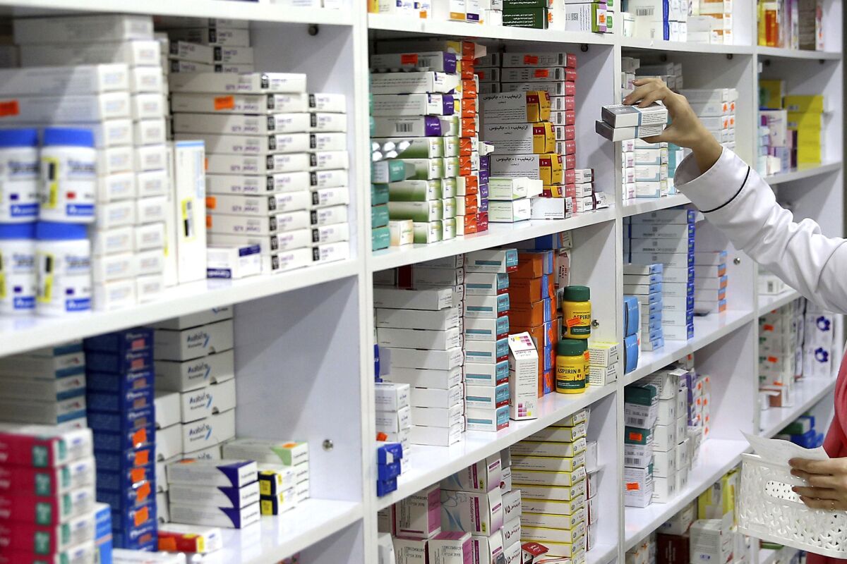 A person in a white coat takes medications from a shelf full of prescription drugs.