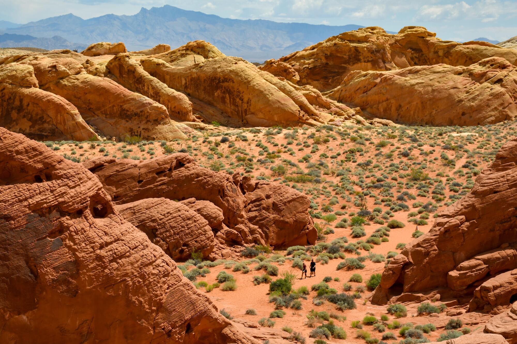 People appear tiny as they walk among reddish-orange boulders and dunes