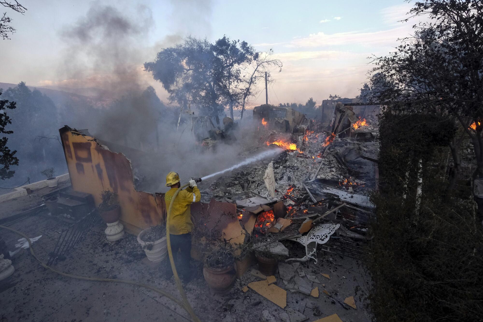 A firefighter aims his hose at flames burning inside a house destroyed by the South fire