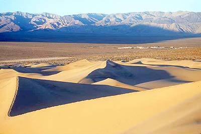 Dunes up to 120 feet high loom in Death Valley National Park, with Stovepipe Wells Village in the background.