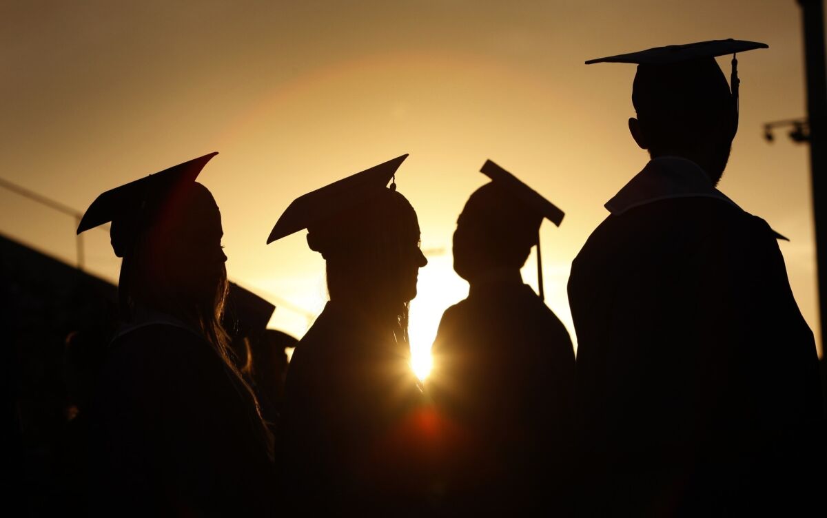 Graduates in caps and gowns gather at sunset