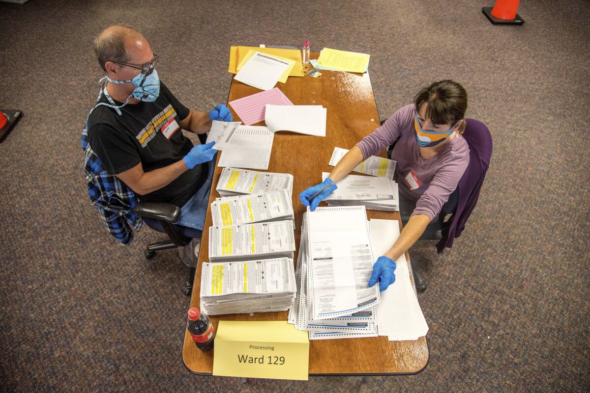 Election workers Jeff and Lori Lutzka, in masks, sit at a table processing stacks of ballots in Milwaukee.