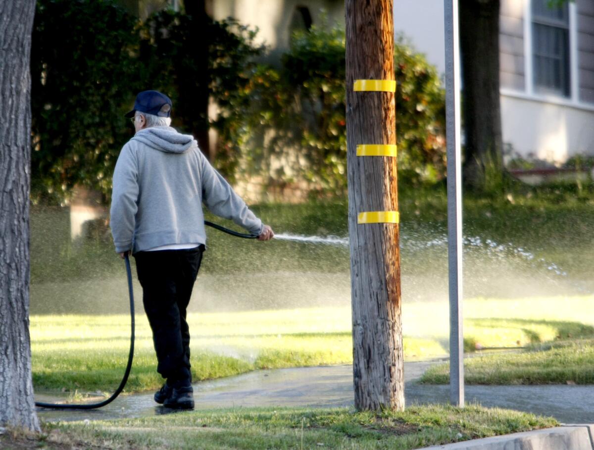 A man waters his lawn with a hose as the sprinklers also water the grass on the 1400 block of Allen Ave. north of Bel Aire Dr. in Glendale on Thursday, April 10, 2014.