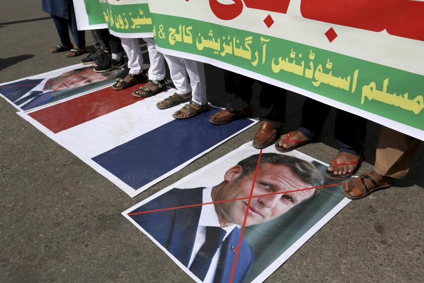 Supporters of the Muslims Students Organization stand on a representation of a French national flag and defaced images of French President Emmanuel Macron during a protest against the president and against the publishing of caricatures of the Prophet Muhammad they deem blasphemous, in Karachi, Pakistan, Friday, Oct. 30, 2020. Muslims have been calling for both protests and a boycott of French goods in response to France's stance on caricatures of Islam's most revered prophet. (AP Photo/Fareed Khan)