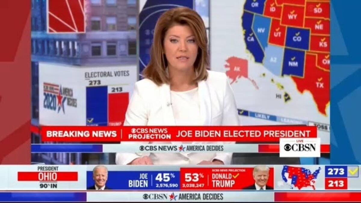 CBS News anchor Norah O'Donnell sits at anchor desk, surrounded by red, white and blue graphics.