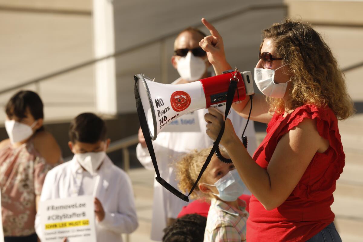 A masked woman with wavy brown hair, in red top and sunglasses, right, holds a bullhorn near other masked people 