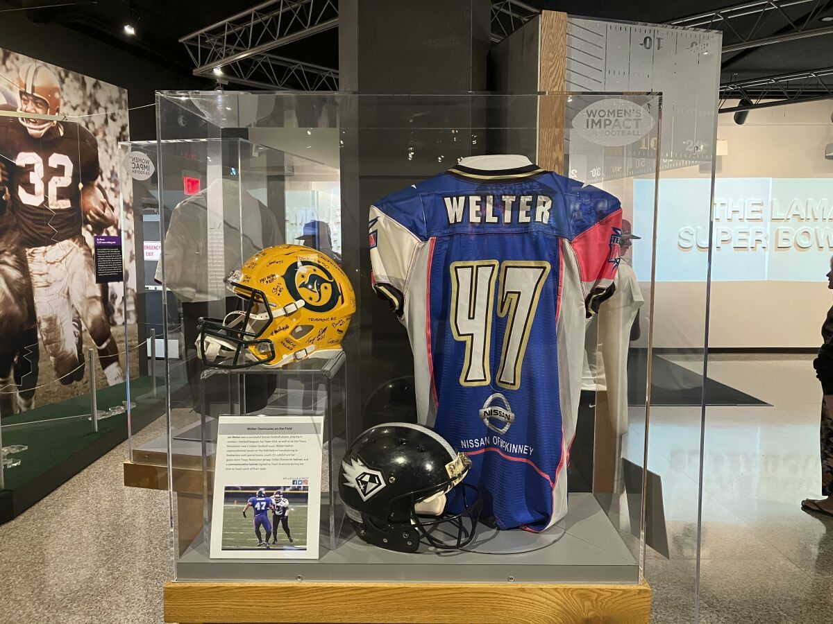 This photo shows a display with Jen Welter's blue-and-pink jersey, Friday, Aug. 5, 2022 in Canton, Ohio. A 15-year-old boy made his way through the The Pro Football Hall of Fame museum on Friday, checking out the memorabilia and bronze busts before stopping to take a picture of Jen Welter’s blue-and-pink jersey to send to his younger sister. (AP Photo/Rob Maaddi)