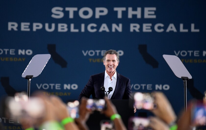 California Gov. Gavin Newsom smiles onstage at a rally against a backdrop reading "Stop the Republican recall"