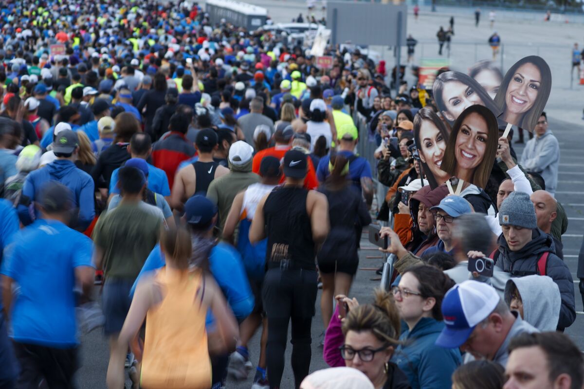 A spectator holds cardboard cutouts of a woman's face as L.A. Marathon runners pass.