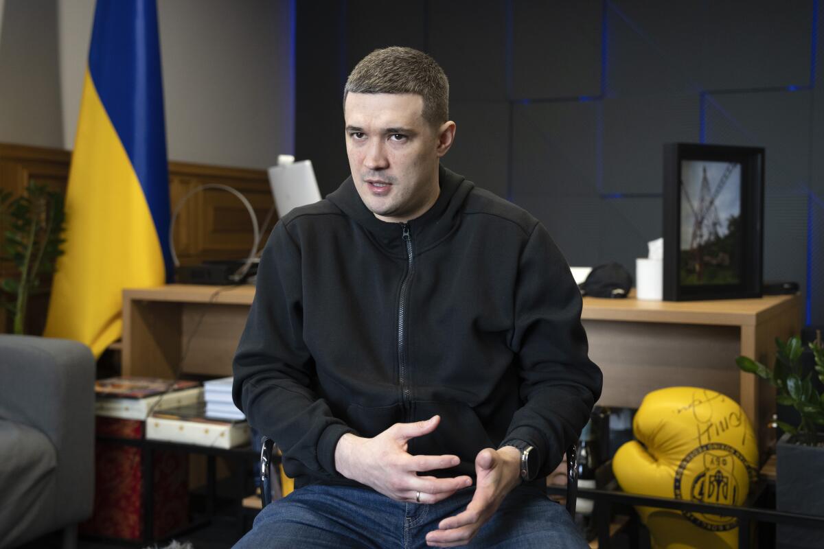 A seated man speaks with a Ukrainian flag in the background