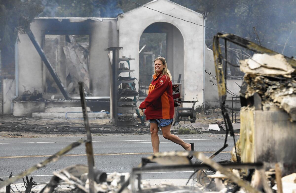 Iona Ridley, 45, wearing donated clothing, walks past the smoldering ruins of Middletown, Calif. She had abandoned her car as the Valley fire approached and was looking to retrieve it. Her home in Cobb Mountain, recently paid off, was destroyed.