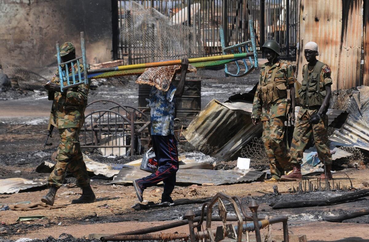 A man carrying a bed walks past South Sudan People's Liberation Army soldiers patrolling the town of Bentiu.