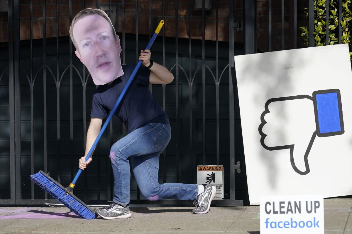 A man holding a broom has a large cutout over his face.