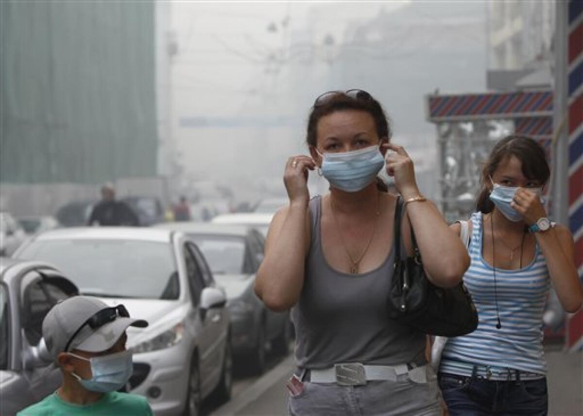 Two women with a boy wear masks protecting from the thickest blanket of smog covering walk through a street as the heavy smog covered Moscow, Russia, early Friday, Aug. 6, 2010. Temperatures up to 100 degrees Fahrenheit (38 C) have exacerbated forest and peat bog fires across Russia's central and western regions, destroying close to 2,000 homes. (AP Photo/Alexander Zemlianichenko)