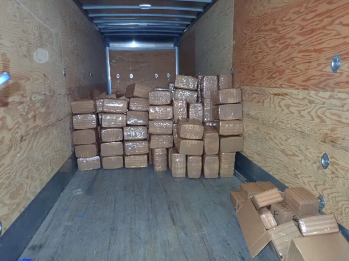 Packages wrapped in brown paper and plastic stacked inside a trailer