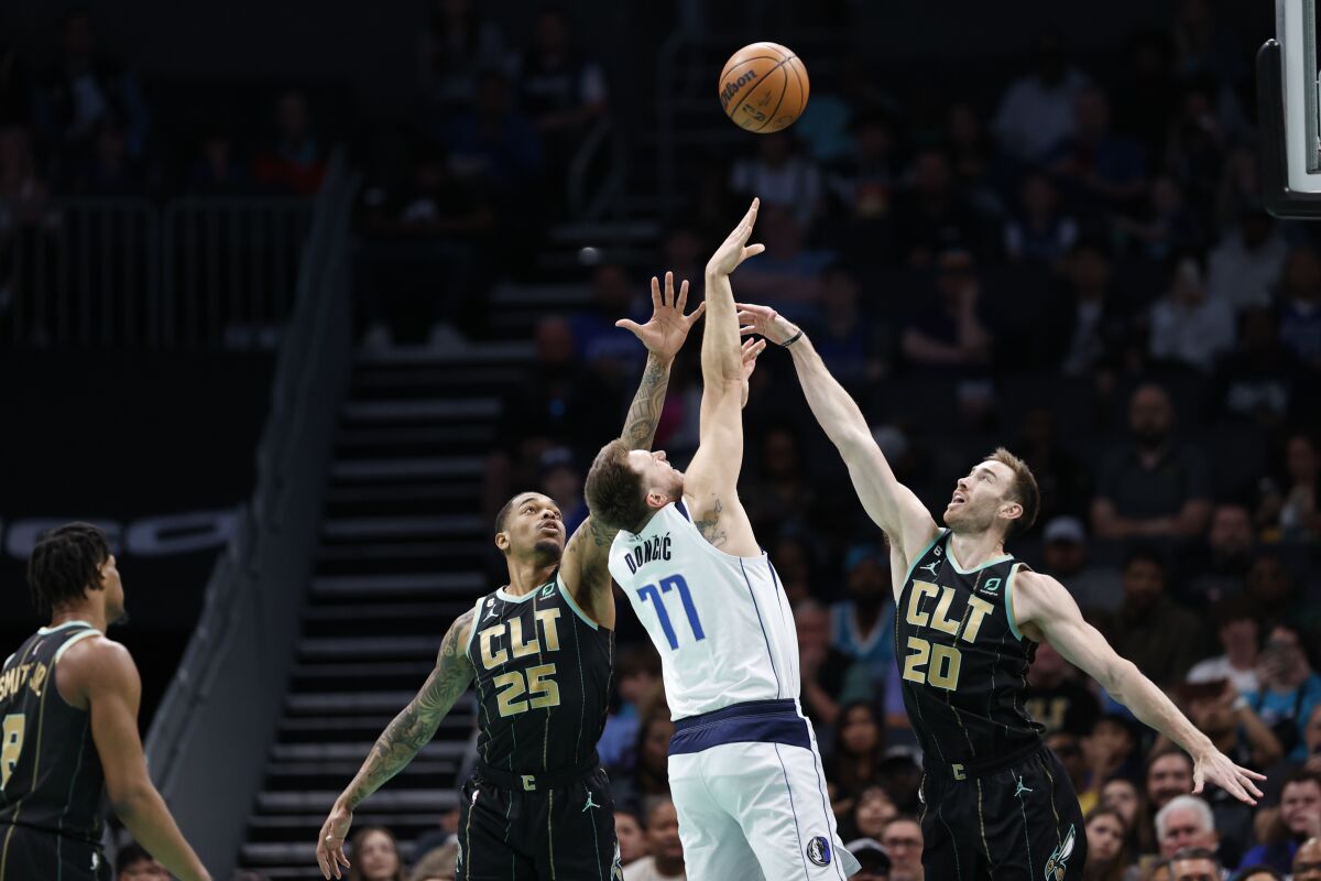 Dallas Mavericks guard Luka Doncic (77) shoots against Charlotte Hornets forwards P.J. Washington (25) and Gordon Hayward (20) during the first half of an NBA basketball game in Charlotte, N.C., Sunday, March 26, 2023. (AP Photo/Nell Redmond)