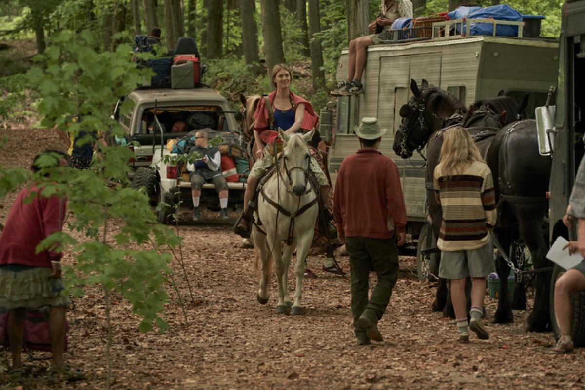 A person rides a horse along a line of parked vehicles on a forest road.