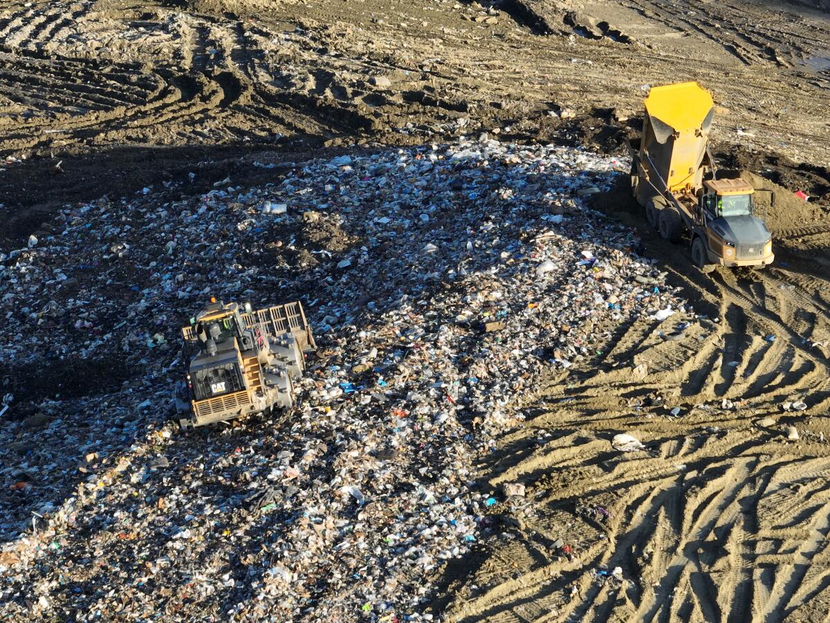 An aerial view of trucks unloading and heavy equipment spreading trash over a hill 
