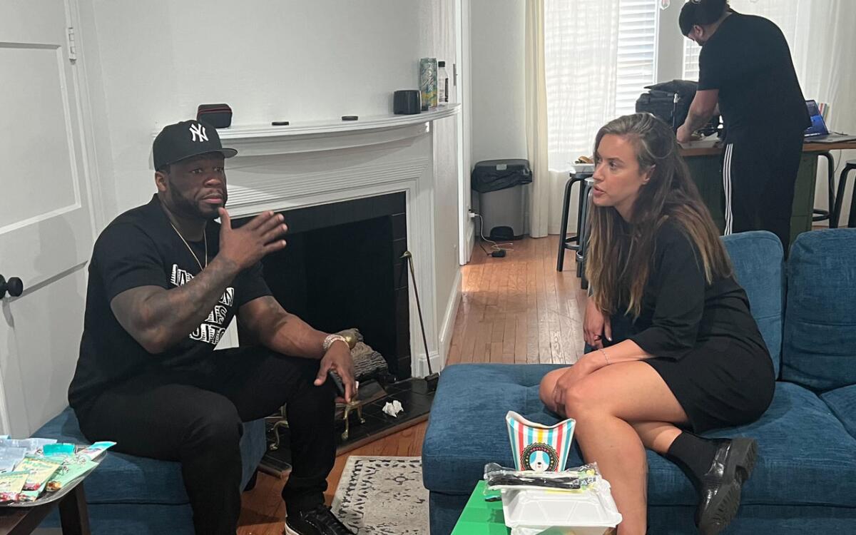 A man in a Yankees cap, left, and a woman sit on couches and talk 