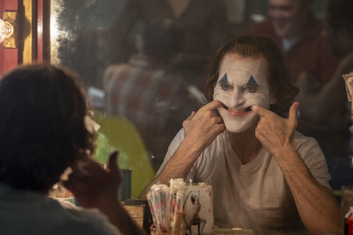 Joaquin Phoenix in "Joker." He is seated and reflected in a mirror, with his index fingers hooked in the sides of his mouth.