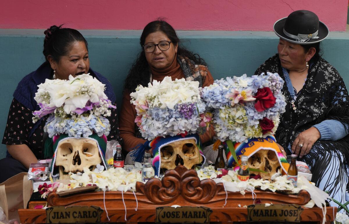 Tres mujeres sentadas con calaveras que han decorado, cada una con una placa con su nombre
