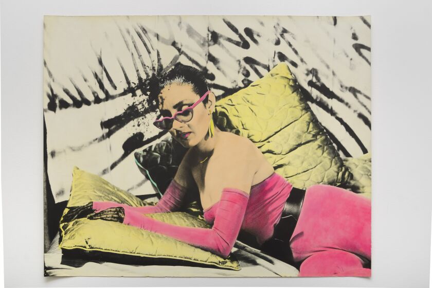 A black and white image show a woman laying on a couch wearing sunglasses, her bodysuit painted a shade of bright pink
