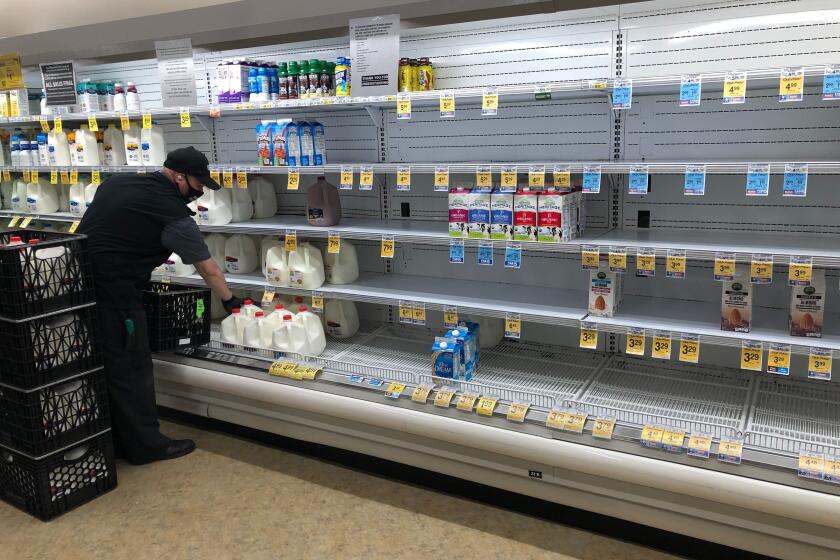 LOS ANGELES, CA - APRIL 7, 2020: A man restocks the milk at a Vons in Los Feliz on April 7, 2020, in Los Angeles, California. Signs around the store announce purchase limit, social distancing guidelines and that no returns are accepted. (Dania Maxwell / Los Angeles Times)