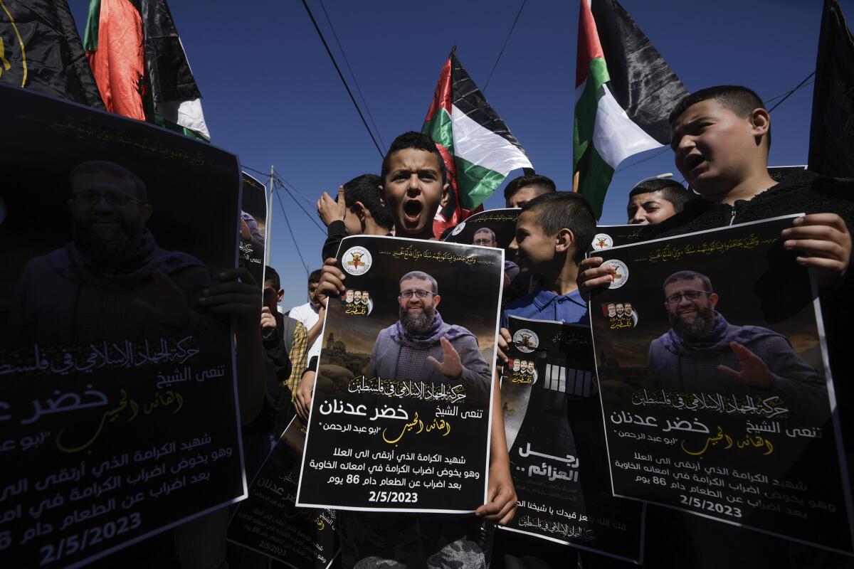 Palestinian kids wave their national flag and hold posters showing Khader Adnan, a Palestinian Islamic Jihad militant