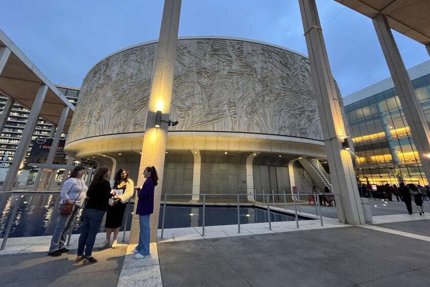 Two women hand leaflets to two theatergoers before the circular architecture of the Mark Taper Forum