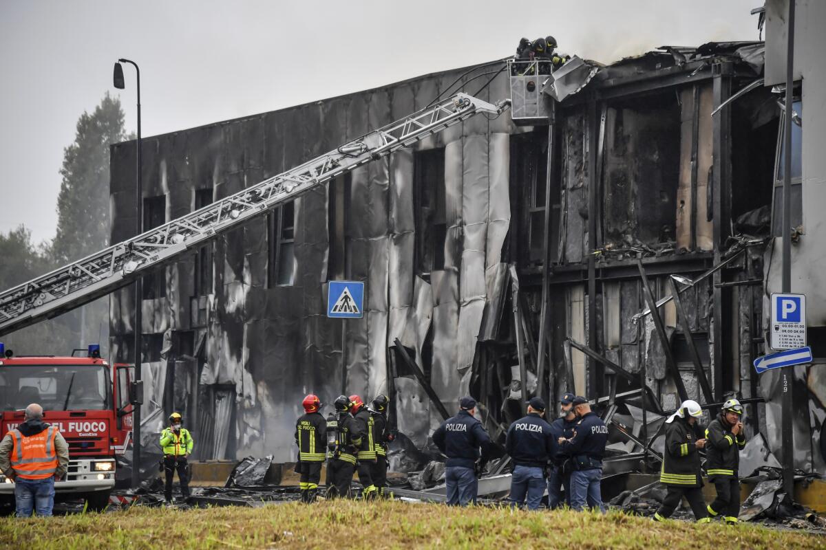 Firefighters work outside a building whose exterior wall is entirely charred