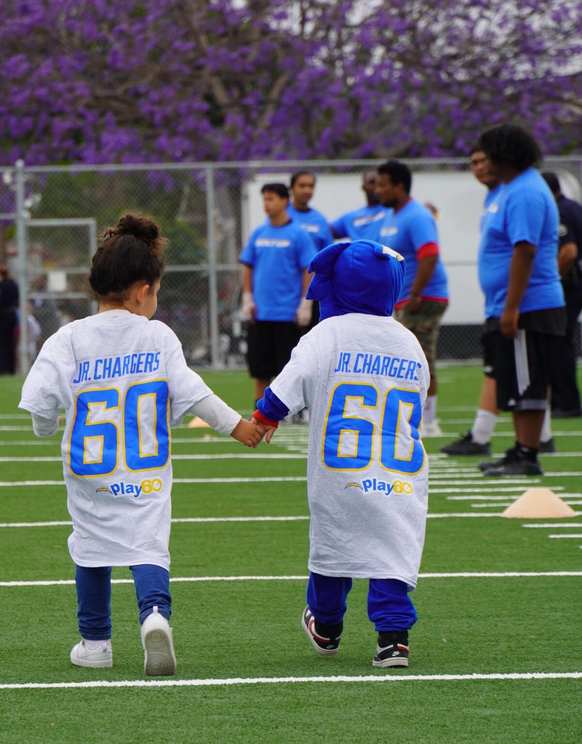 Two children in oversize jerseys hold hands.