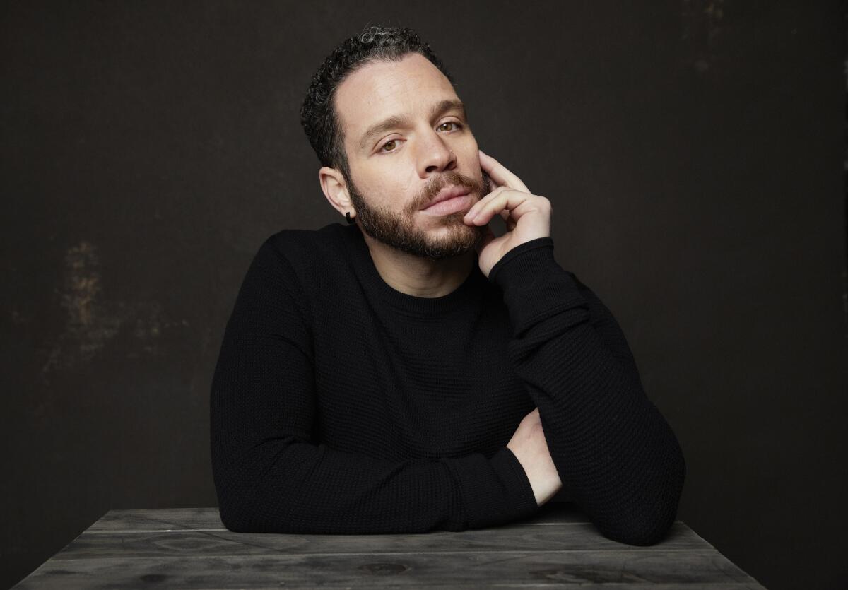 Actor Robin de Jesus sits at a table with his hand on his chin.