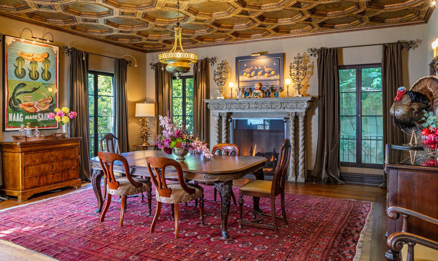 The dining room with a dining set, chandelier, rug, fireplace and windows overlooking greenery.