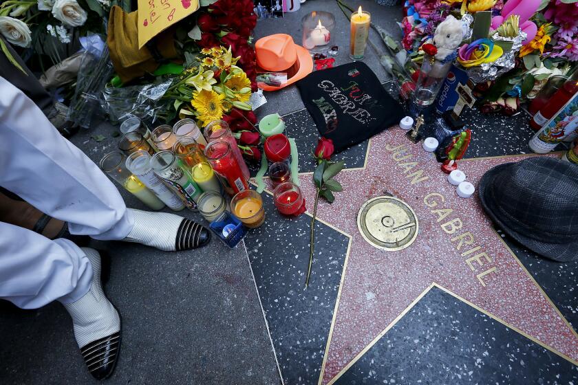 A fan of Mexican pop singer-songwriter Juan Gabriel stands next to his star on the Hollywood Walk of Fame, which was turned into an impromptu memorial. Juan Gabriel died Sunday at age 66.