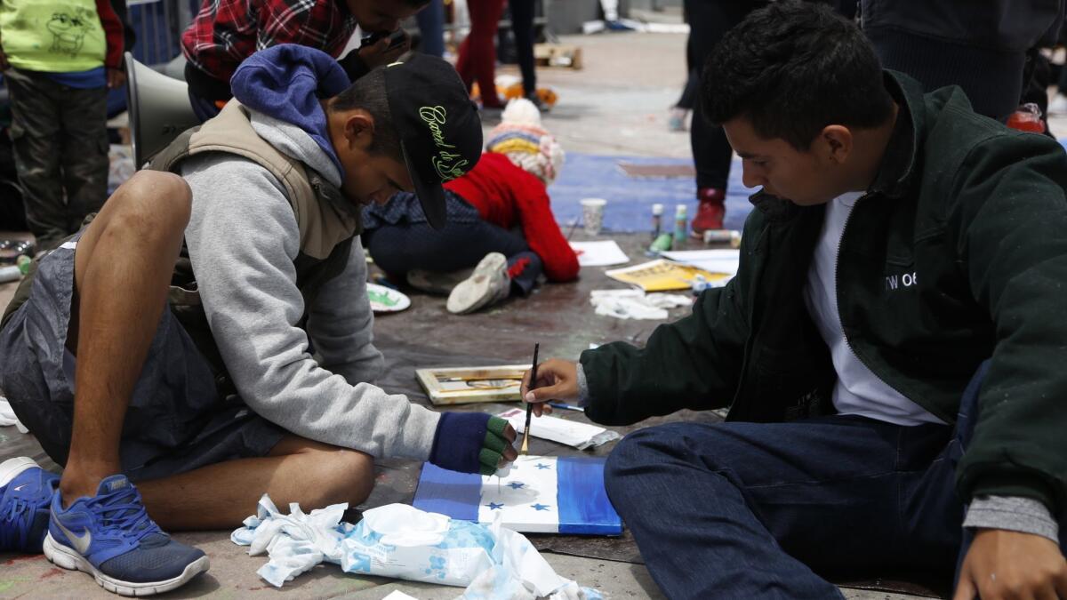 Alejandro, left, of El Salvador, and Jose, of Honduras, paint a Honduran flag while awaiting entry into the U.S.