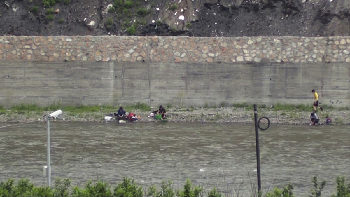 North Koreans are seen on the edge of a river on the border with China, guarded in part by a security camera.
