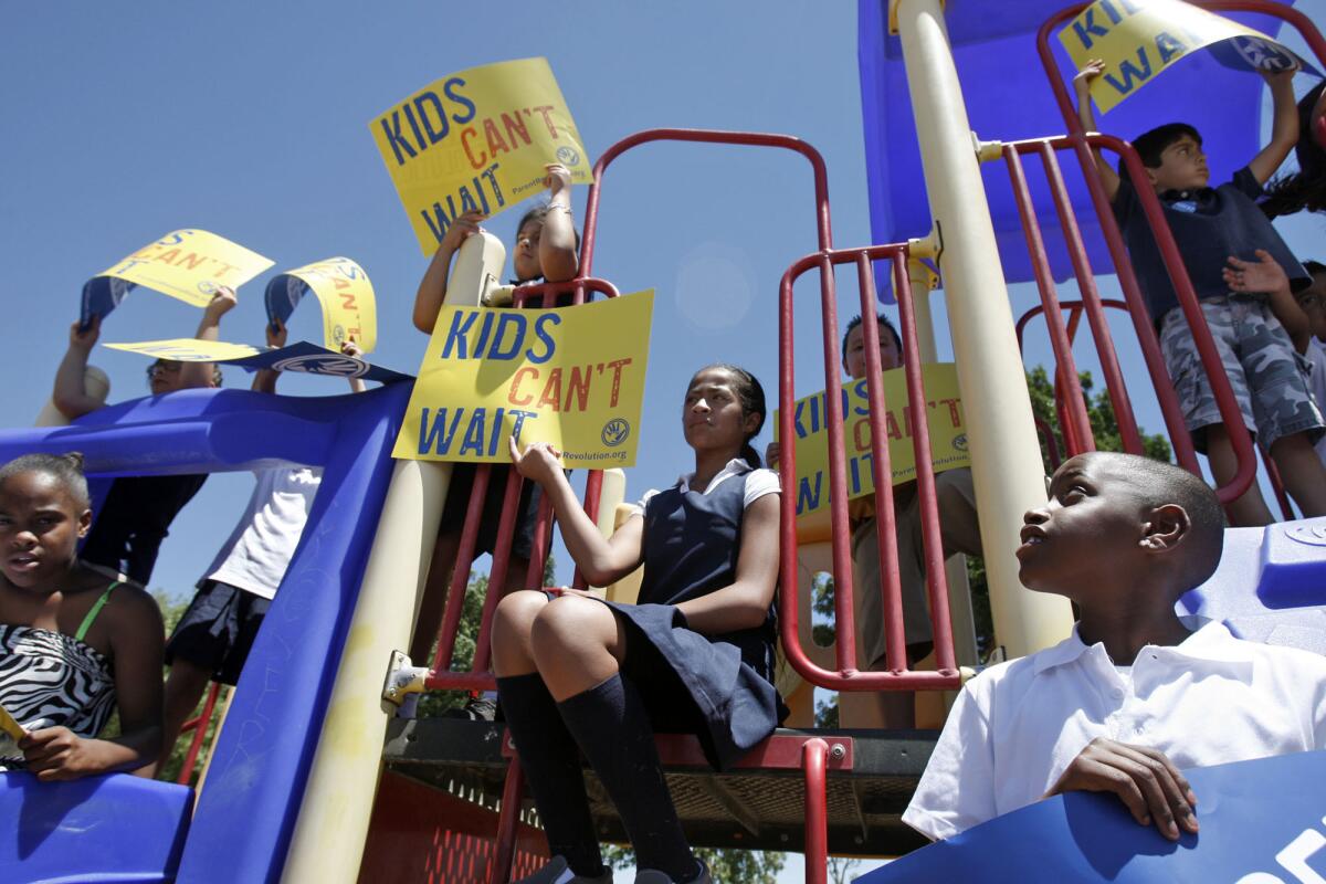 Aubrey Abner, far right, 9, and other children hold "Kids Can't Wait" signs on opening day of the Desert Trails Preparatory Academy in Adelanto, Calif. Two mothers charged with vandalizing the school after losing a battle to stop it from becoming a charter have pleaded not guilty.