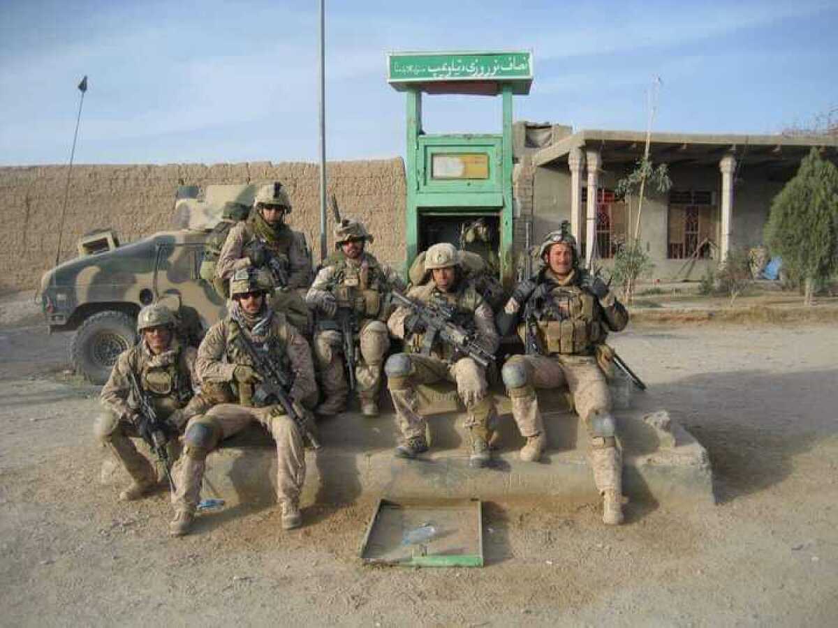 A group of U.S. Marines poses near a military vehicle in a dusty land