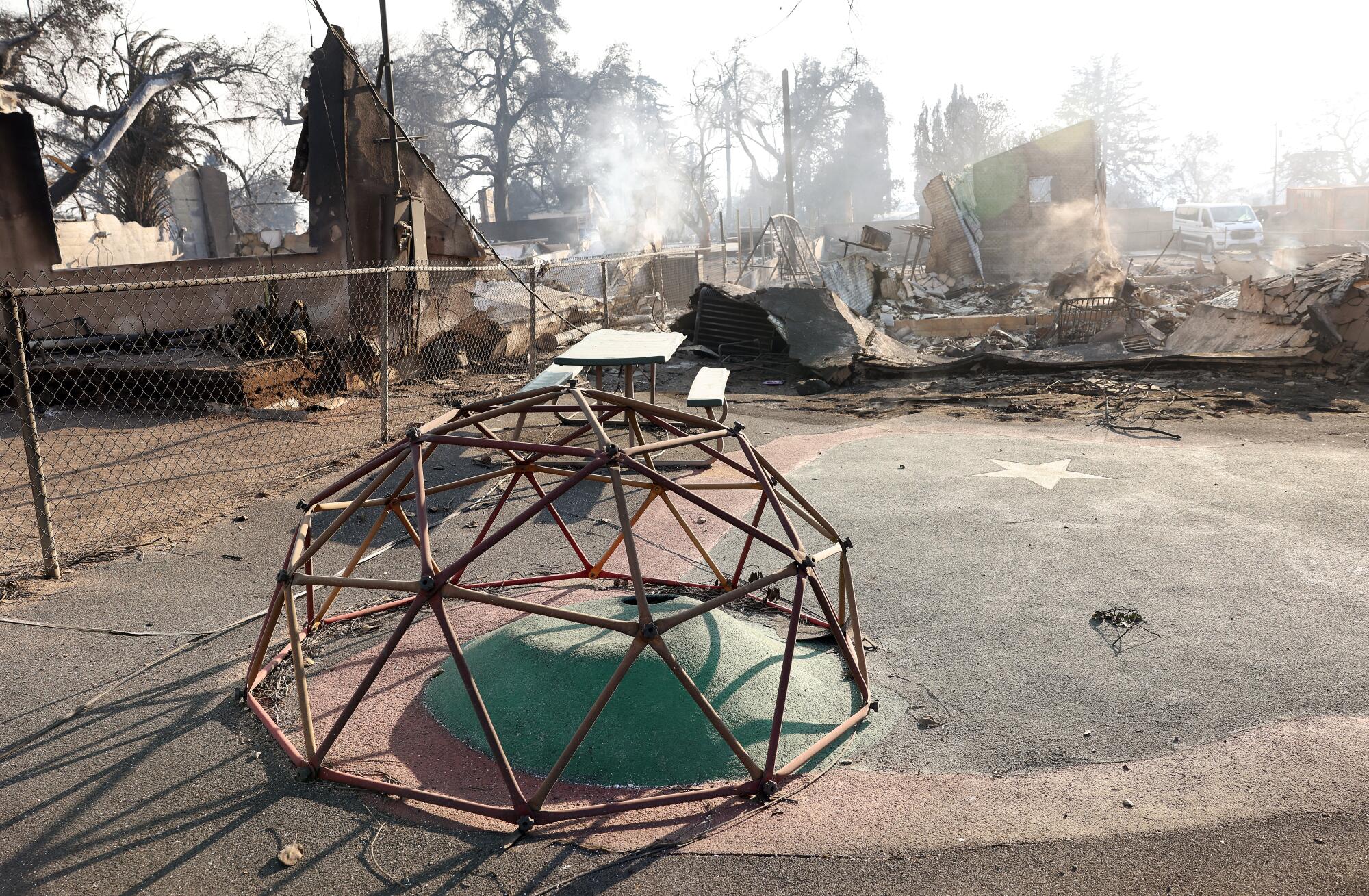 A climbing dome stands amid a burned playground,
