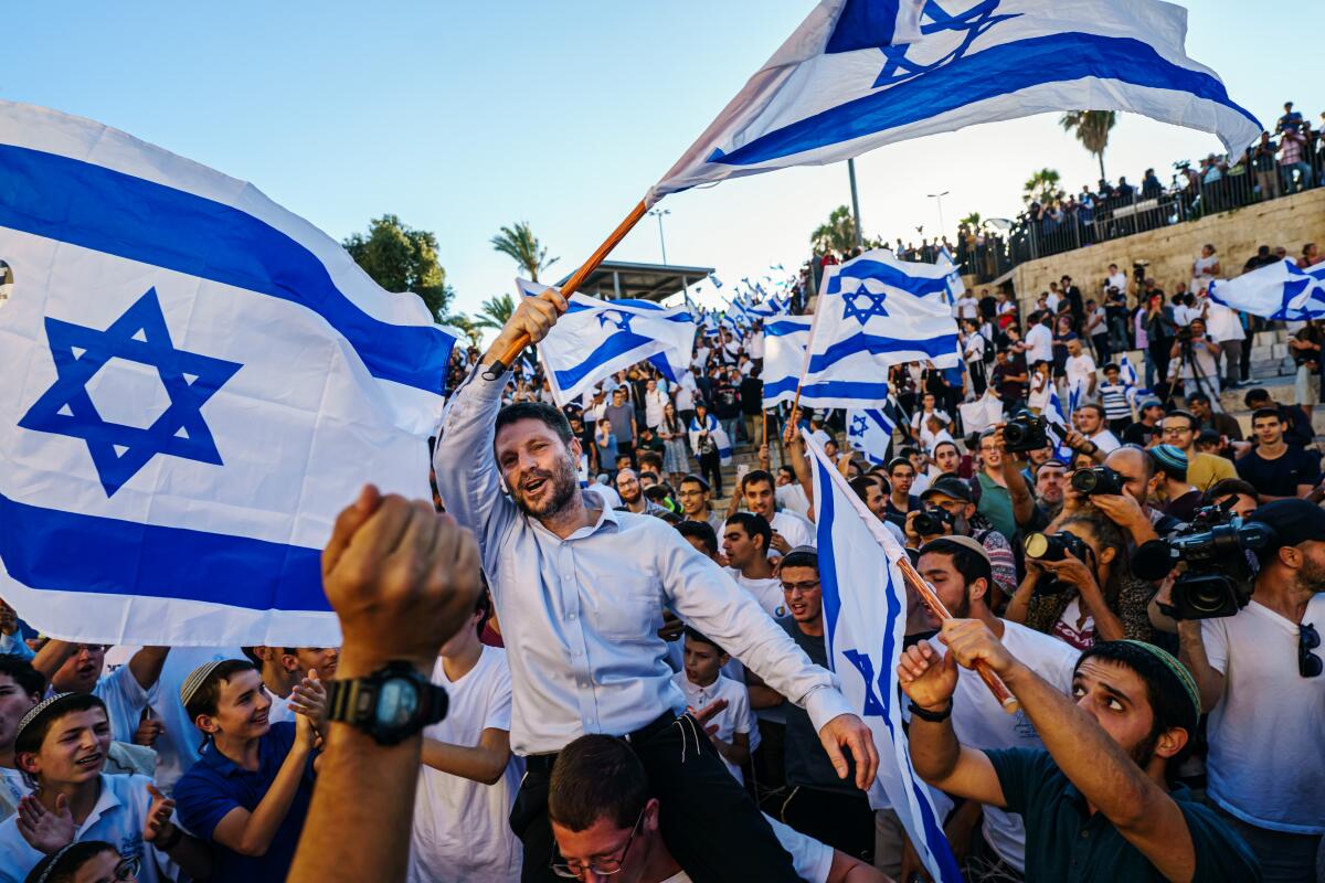 A man waving an Israeli flag is carried by a crowd of people, many also waving flags.