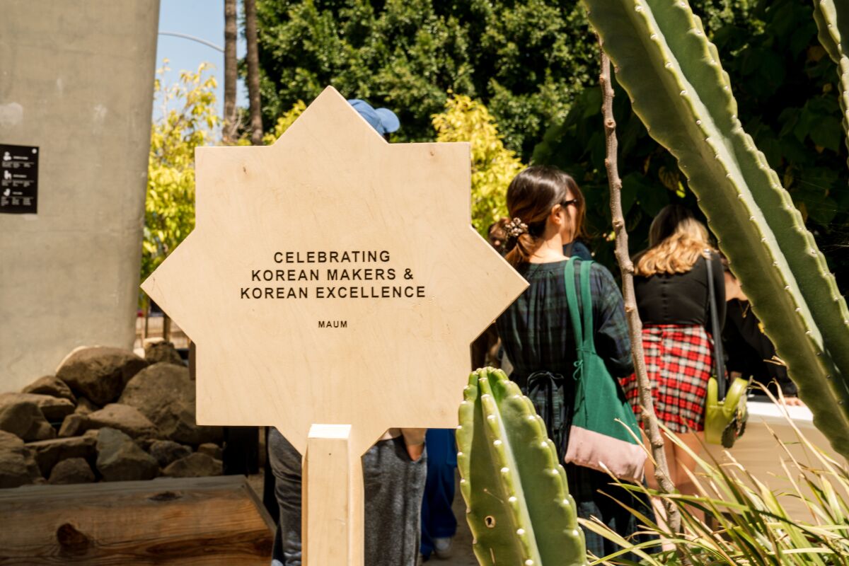 A sign that reads "Celebrating Korean Makers and Korean Excellence" surrounded by cactus and people.