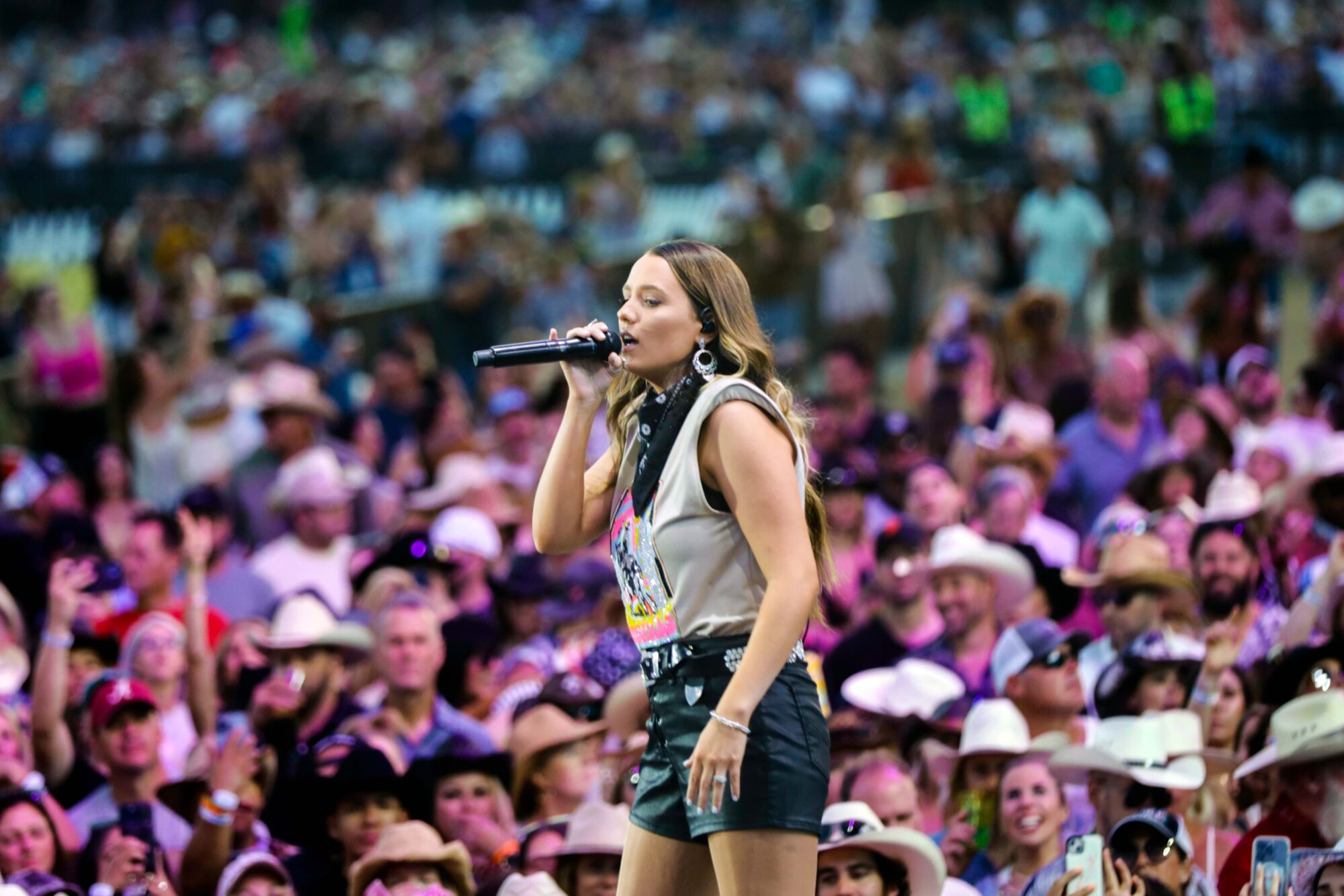A woman sings into a microphone while a crowd is behind her.
