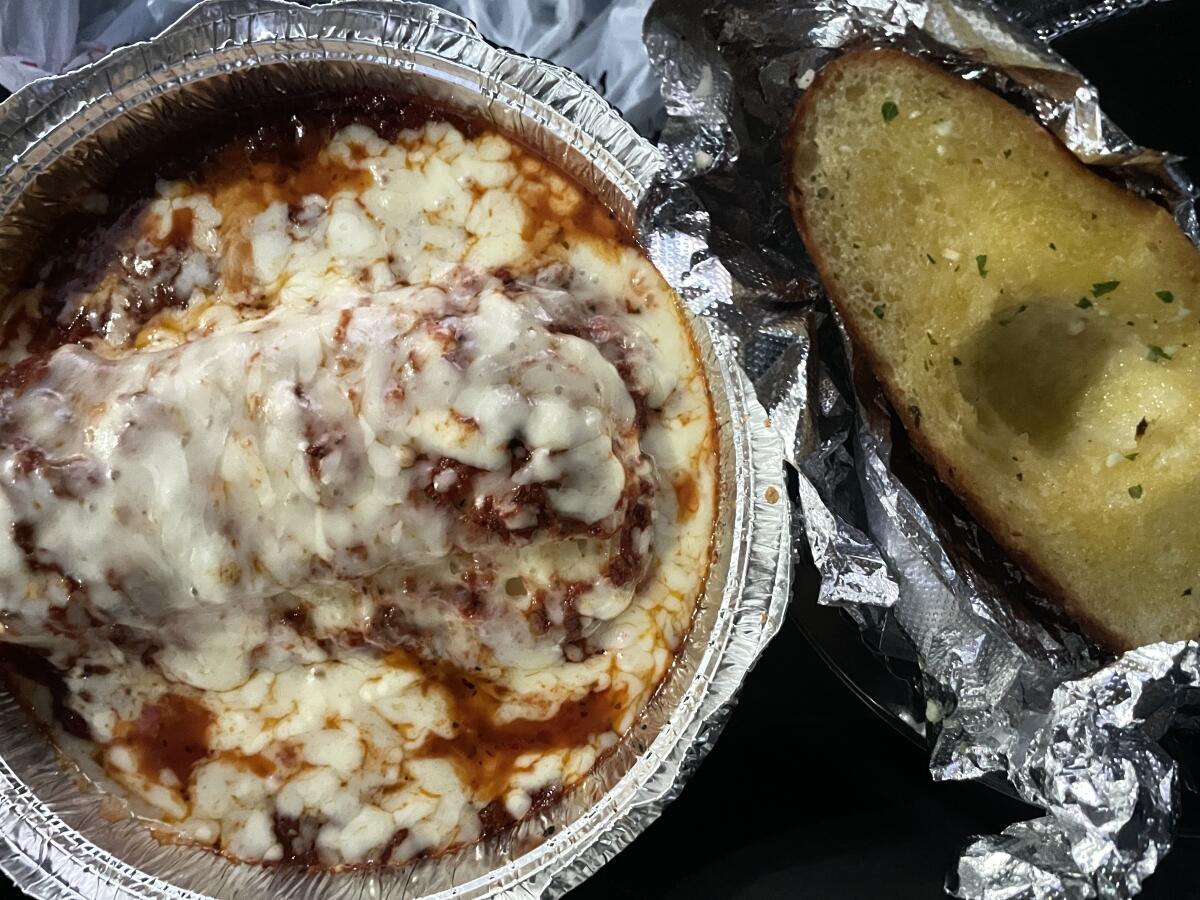 A container of lasagna and garlic bread.