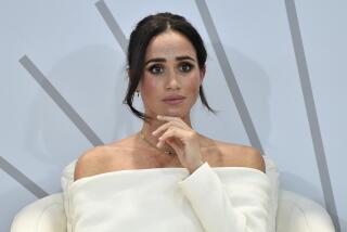Meghan, Duchess of Sussex, sits in a white chair and stares pensively ahead while wearing a white outfit.