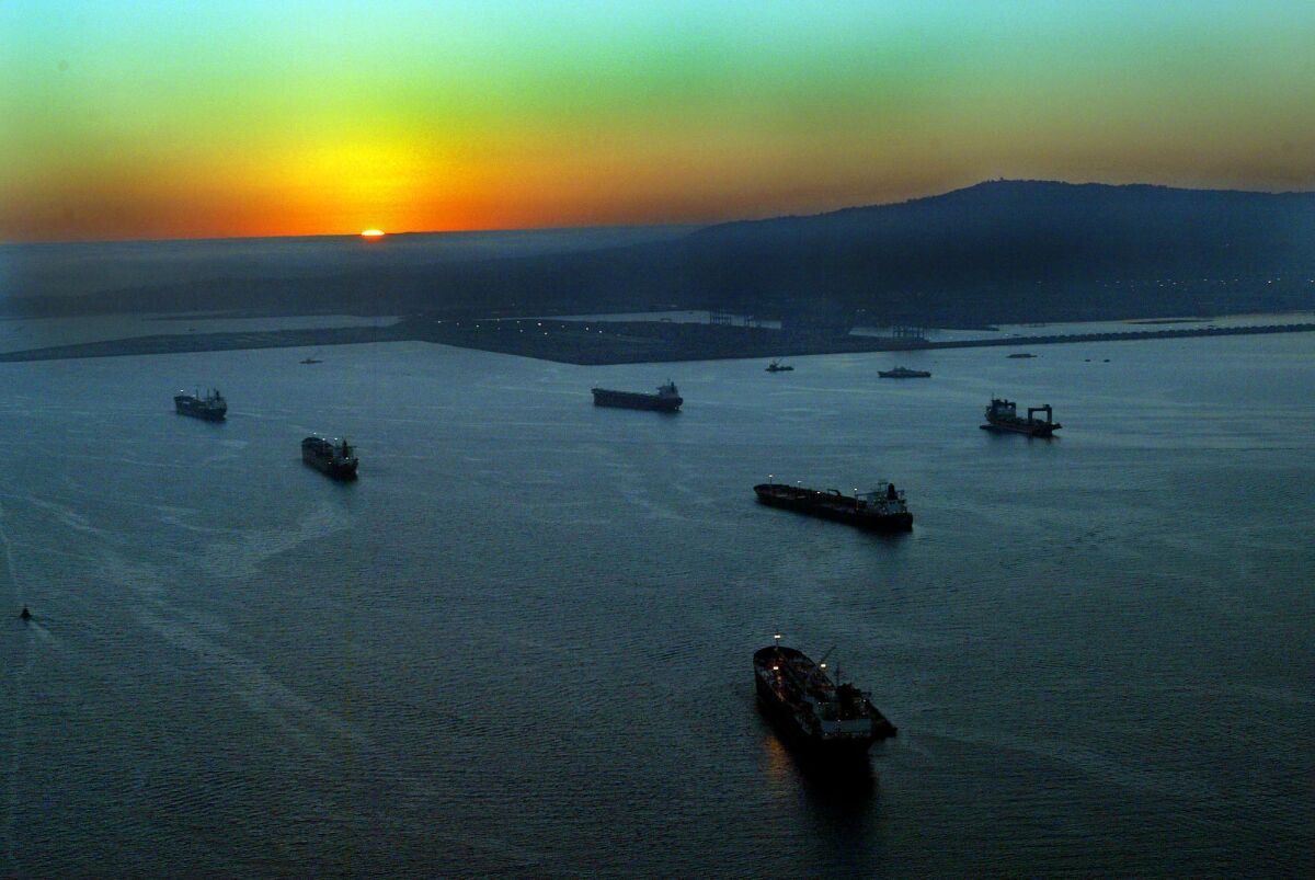 Cargo ships line up to enter the Port of Los Angeles as the sun sets over the Pacific Ocean.