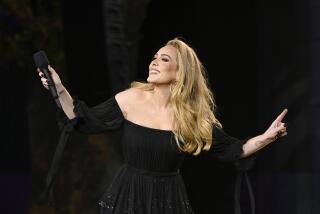Adele smiles and holds a microphone while wearing a black dress.