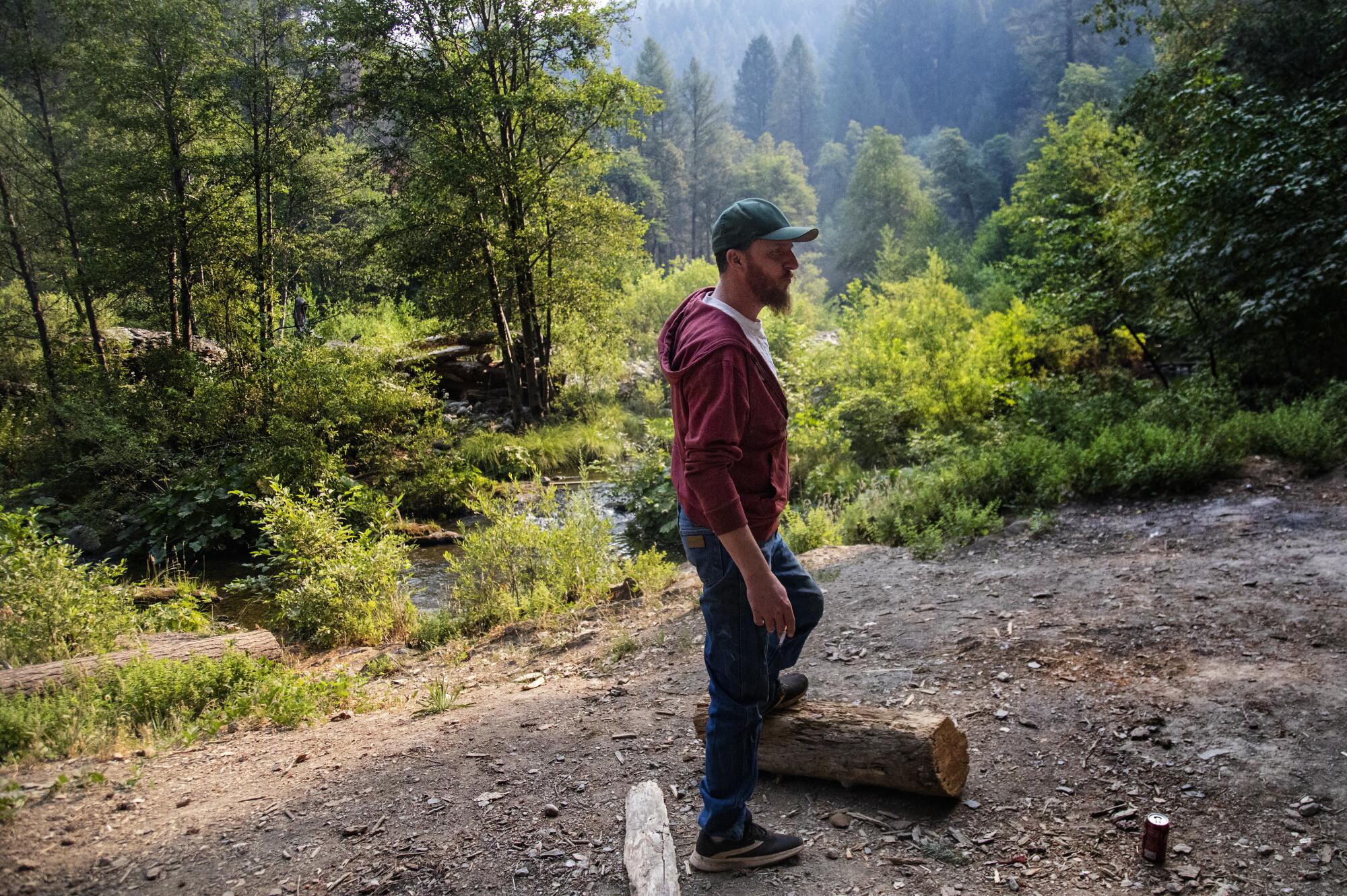 Jedediah Anderson stands with his foot on a log at a wilderness campsite.