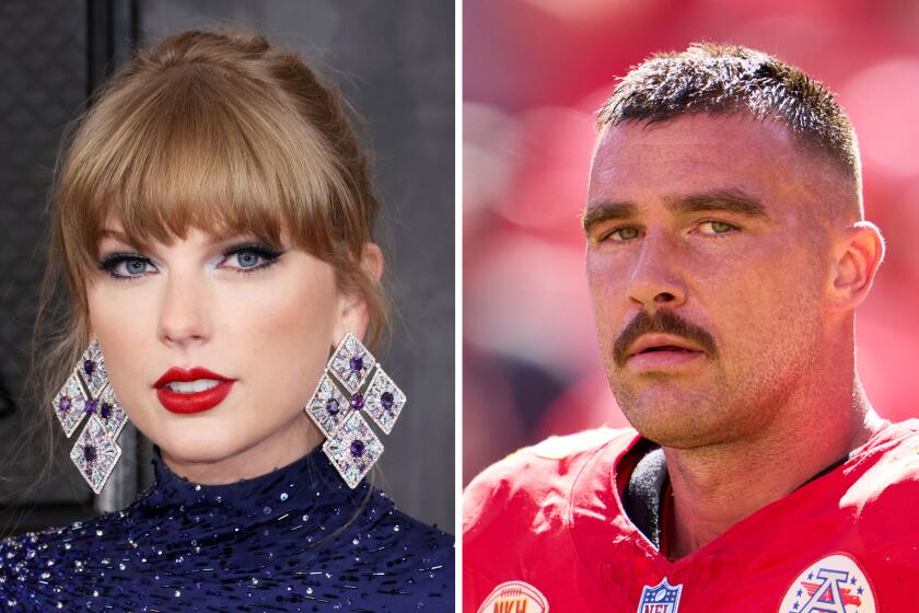 Taylor Swift in a blue turtle neck dress and big dangling earrings and Travis Kelce in a Kansas Chiefs uniform