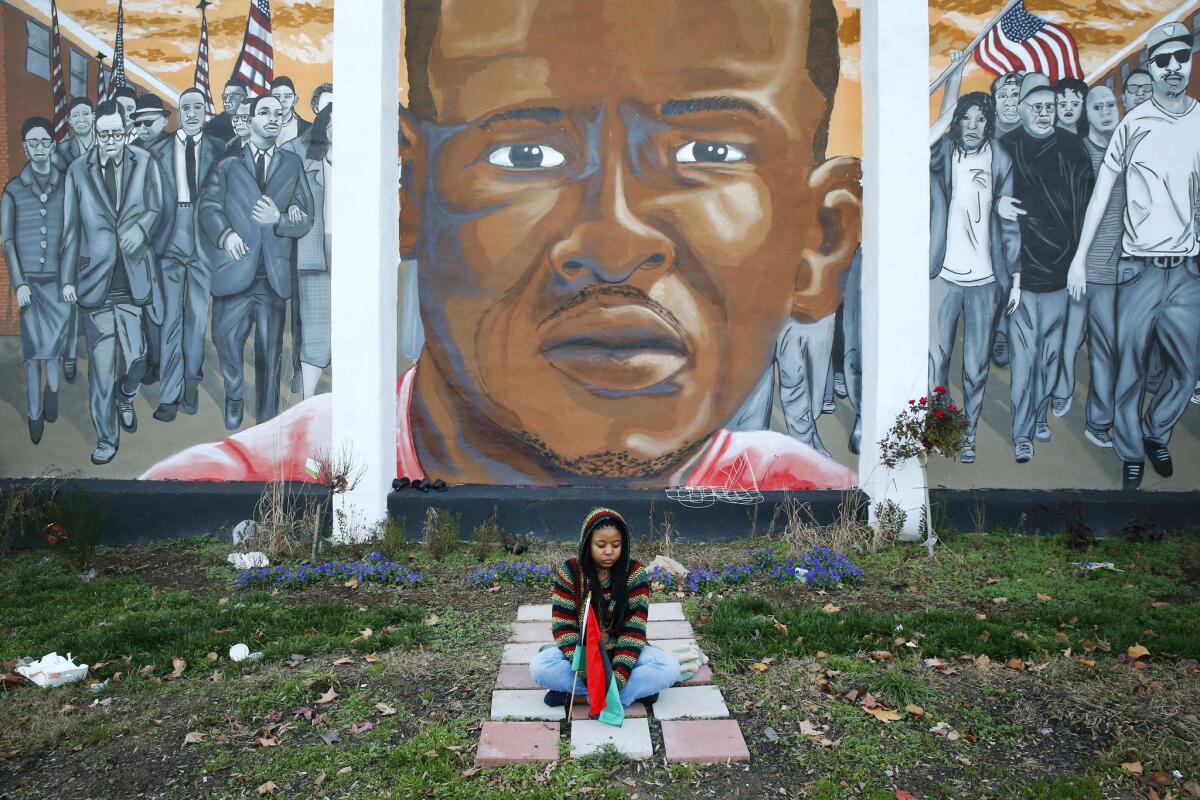 Jazmin Holloway sits in front of mural depicting Freddie Gray