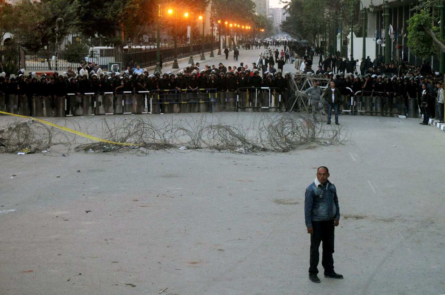Egyptian police look on as a man watches protesters pull down the protective barricade made of cement blocks along Qasr el-Eine street which lead to Tahrir Square, the epicenter of the Egyptian revolution which saw last year's overthrow of president Hosni Mubarak